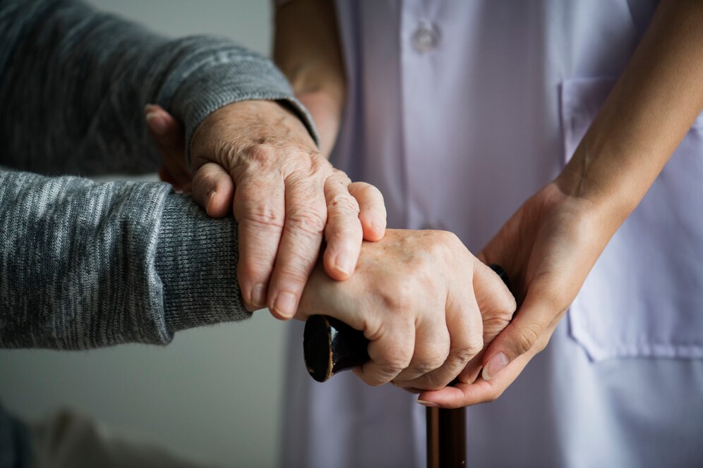 Abandono de Incapaz em condomínio: mãos idosas segurando bengala enquanto cuidadora dá suporte