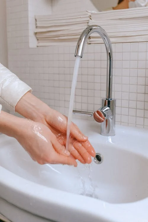 Aproveitamento da água da chuva em condomínios: pessoa usando torneira para lavar as mãos no banheiro