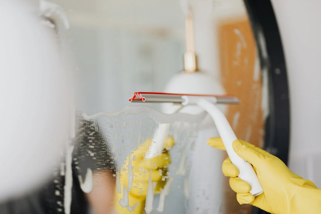 Aproveitamento da água de chuva em condomínios: pessoa limpando espelho com rodo e luva amarela