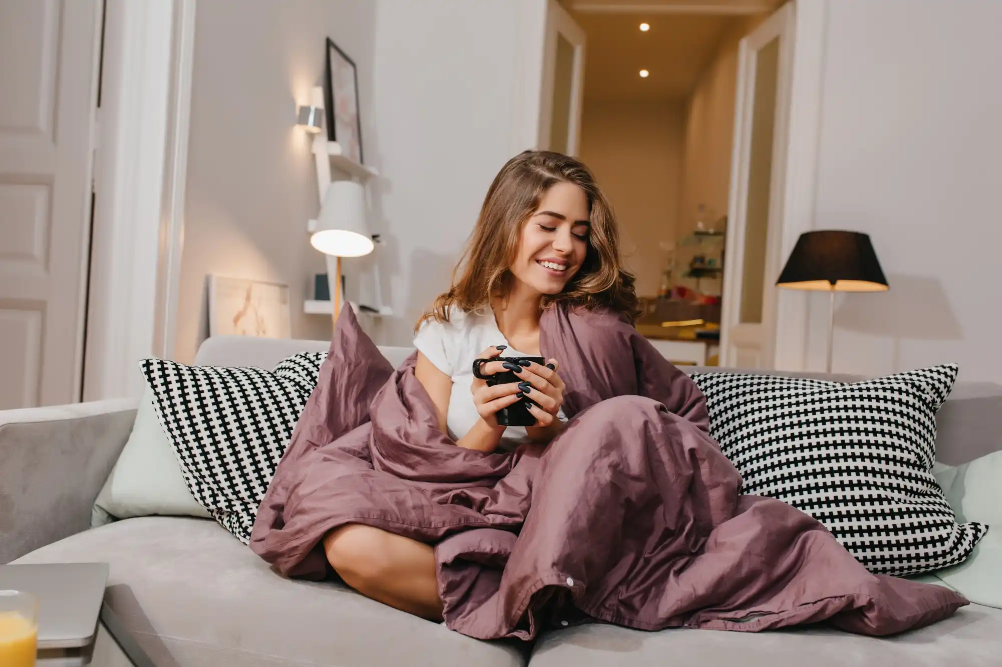 Casa aconchegante no inverno: mulher com roupas de frio enquanto toma uma bebida quente.