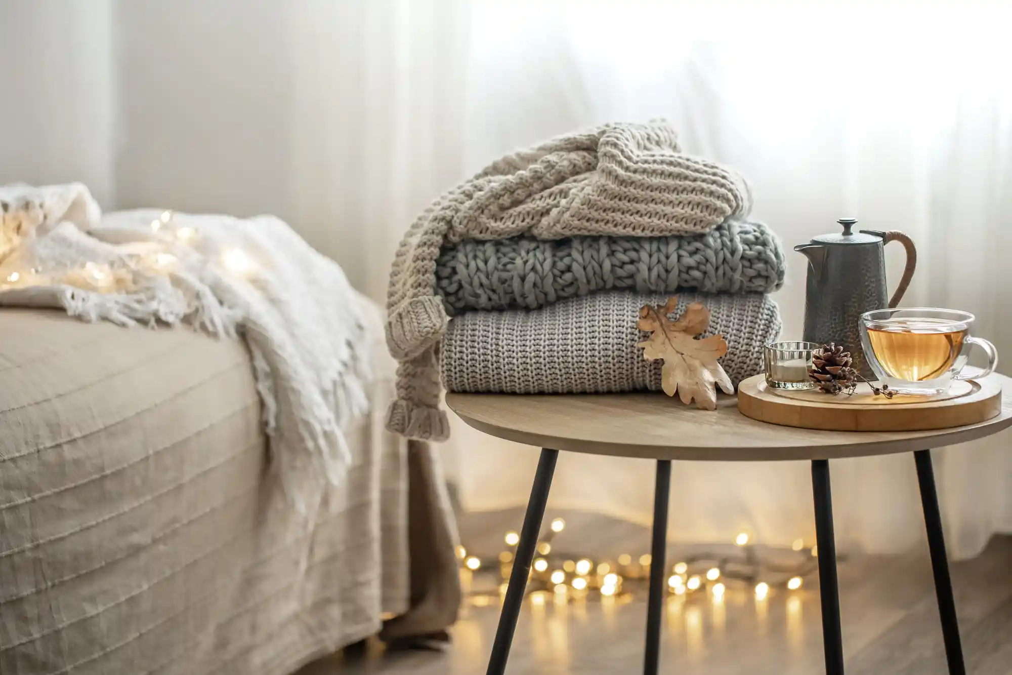 Casa aconchegante no inverno: foto de casacos empilhados, com chá e, ao lado, uma cama com cobertas.
