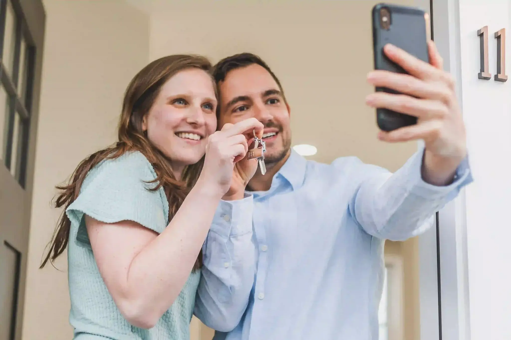 Comprar imóvel pra investir: casal tirando selfie enquanto mostra as chaves da casa nova