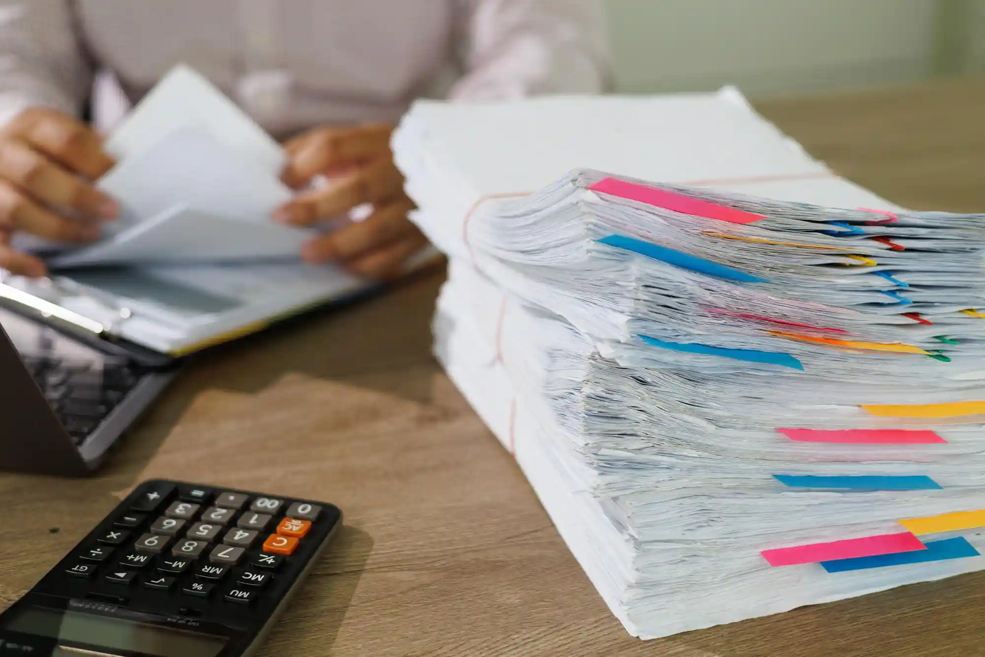 Dívida de condomínio: pessoa segurando papéis perto de calculadora, notebook e pilha de folhas com adesivos