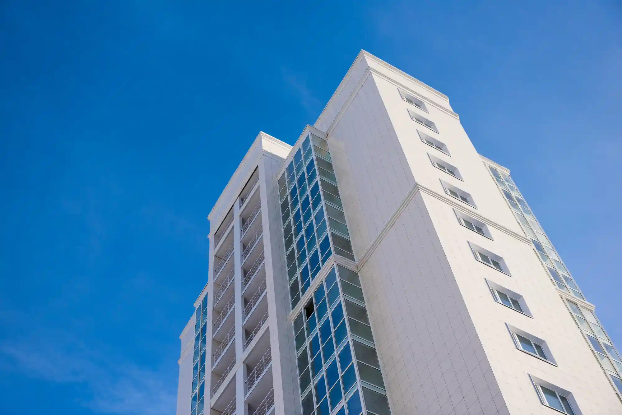 Fachada de condomínio: imagem de baixo para cima de um prédio branco com detalhes azuis, junto com o céu azul