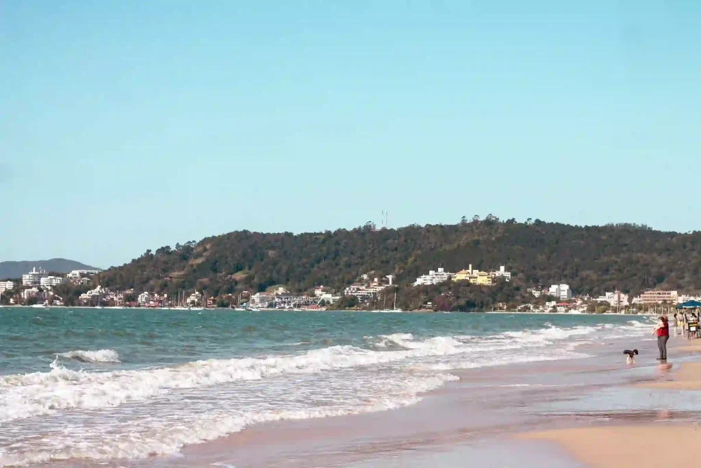 Morar em Jurerê: imagem da praia do forte em um dia sem nuvens, com areia, água e montanhas