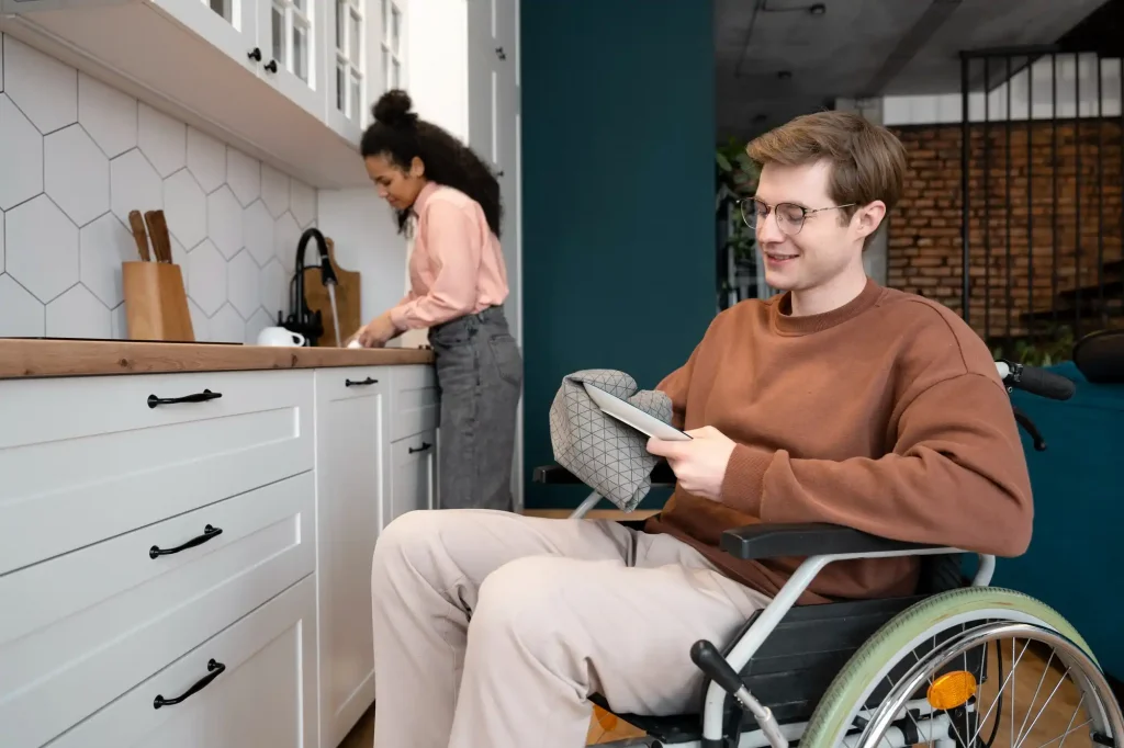 Lei da acessibilidade: homem com deficiência em cadeira de rodas, na cozinha, ao lado de amiga