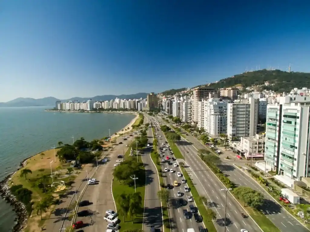 Morar em Florianópolis: imagem aérea de uma das avenidas da cidade, com 4 faixas de carros e perto do litoral, com mar e prédios