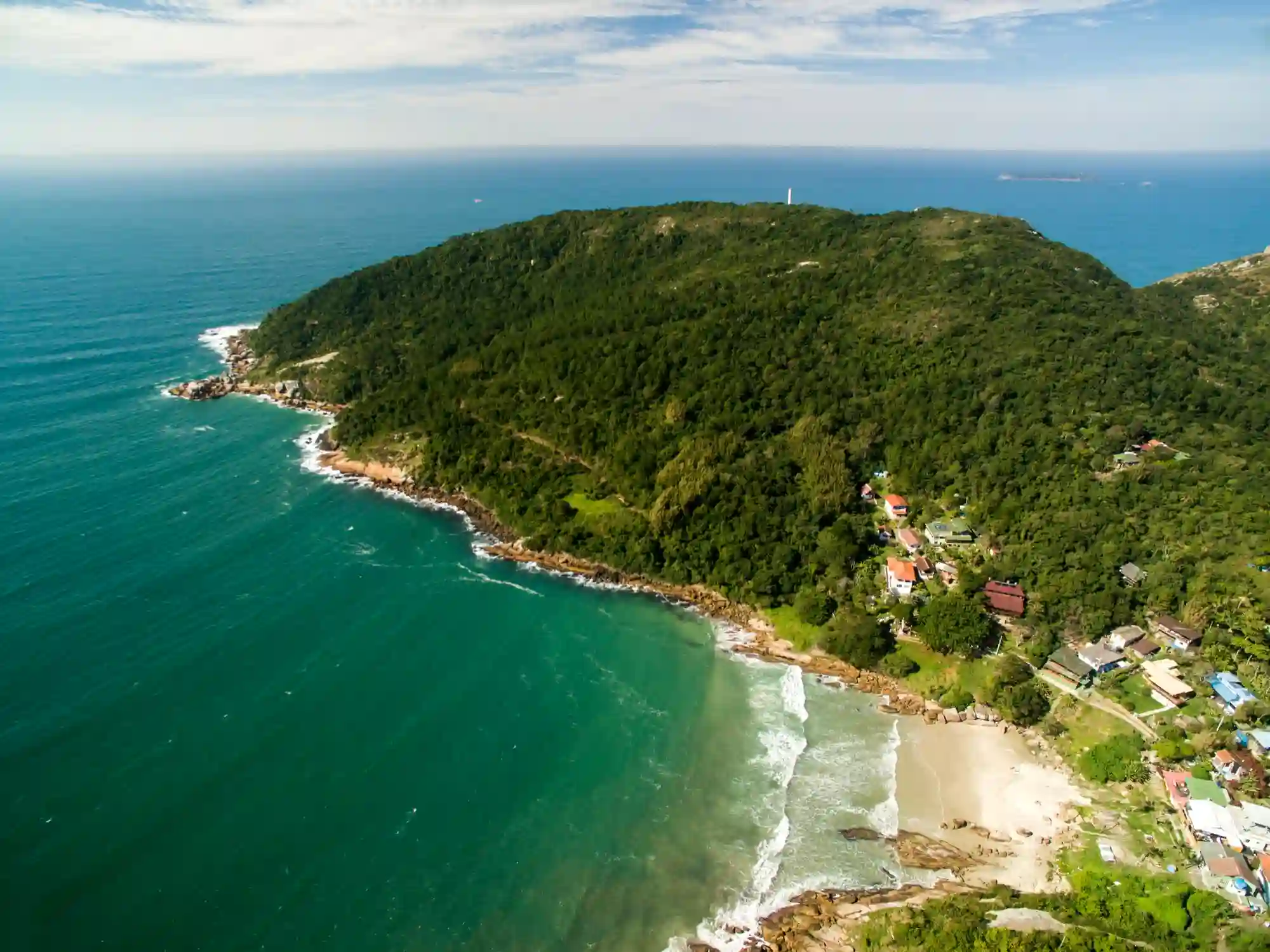 Morar em Florianópolis: imagem aérea do litoral da cidade, com residências, grande área verde e praia