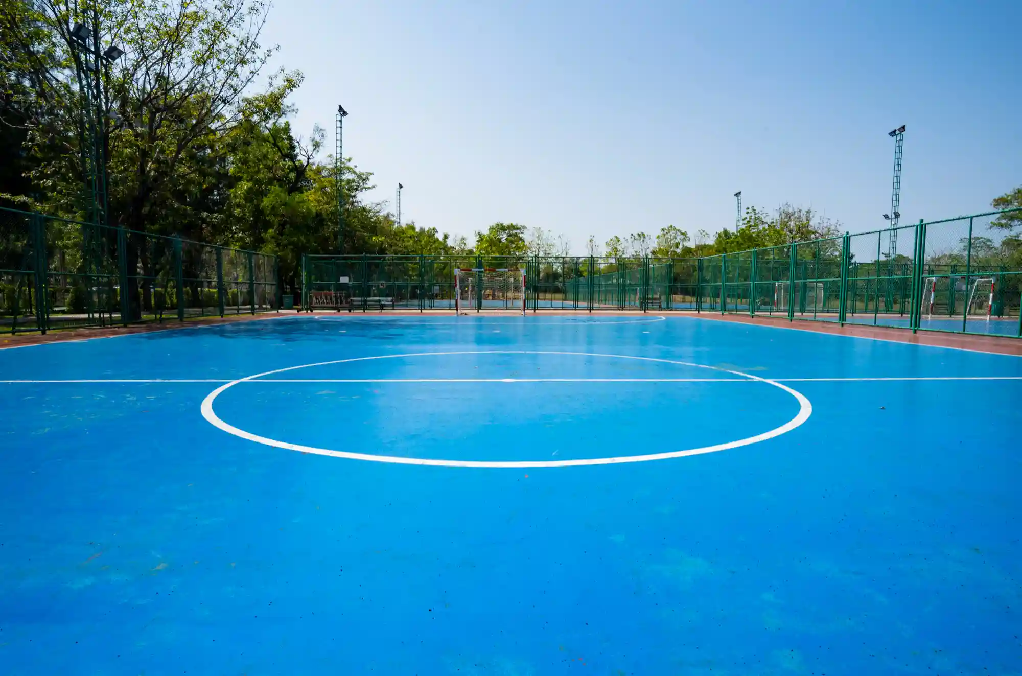 Imagem de quadra poliesportiva azul, próximo a um parque