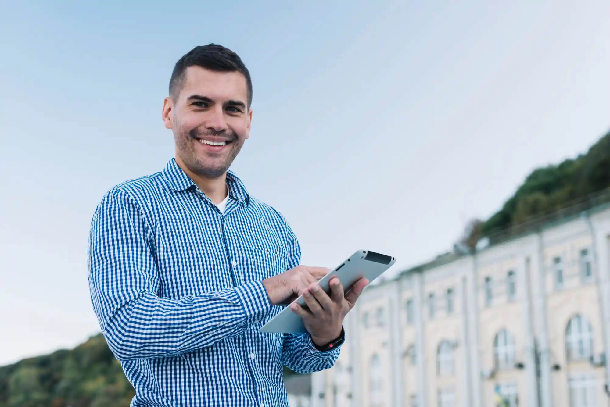 Subsíndico: homem do lado de fora do condomínio sorrindo e com tablet na mão
