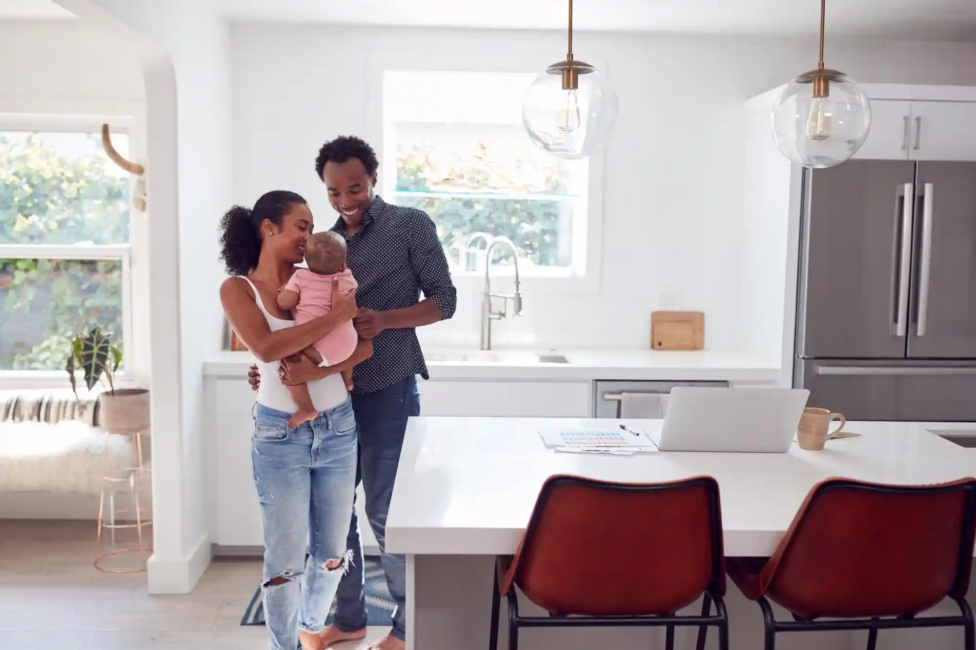 5 Melhores tipos de imóveis para viver a dois: imagem de casal com bebê em sua casa, com cadeiras, mesas, geladeira e espaço integrado.