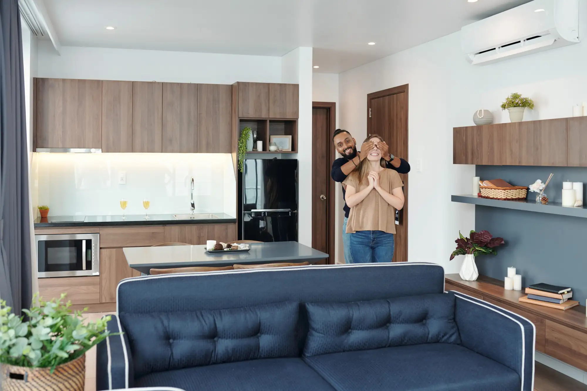 5 Melhores tipos de imóveis para viver a dois: homem tapando os olhos da mulher para mostrá-la o novo loft de ambiente integrado com sofás, estantes e cozinha americana.