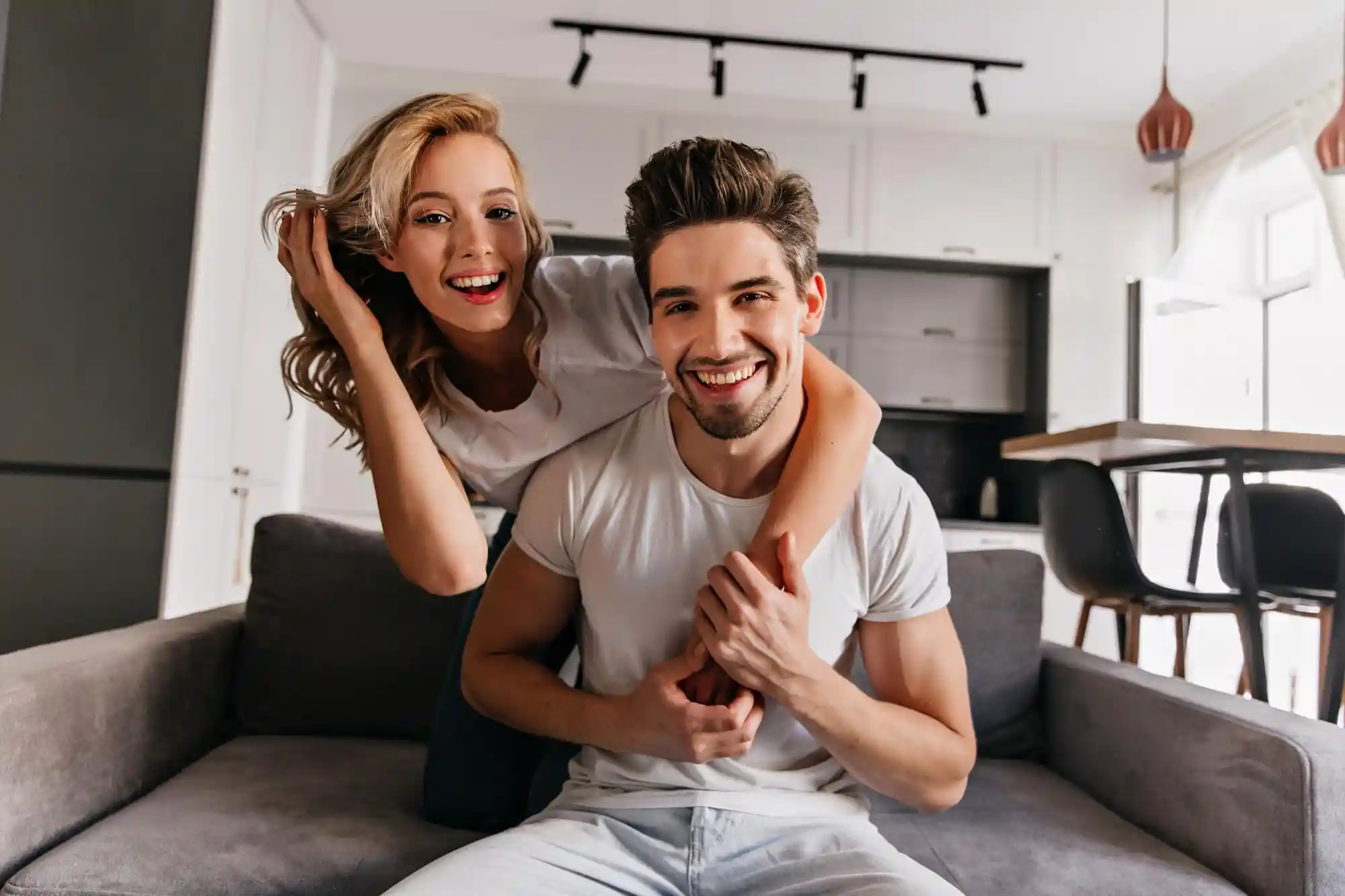 5 Melhores tipos de imóveis para viver a dois: imagem de casal sorrindo no sofá da sua kitnet.