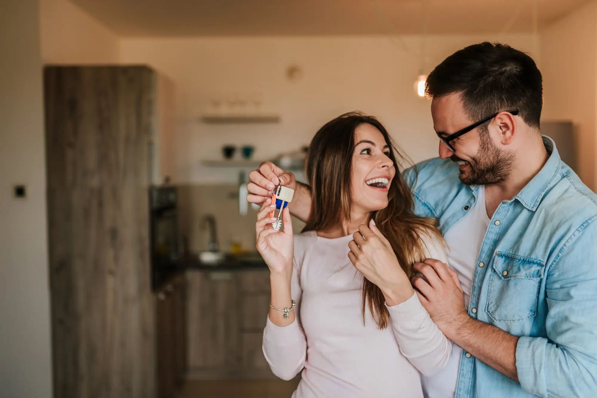 5 Melhores tipos de imóveis para viver a dois: casal se abraçando com a cozinha do imóvel ao fundo